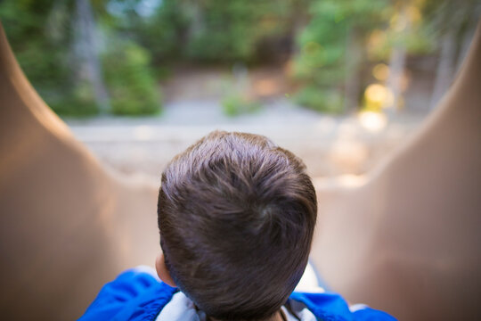 Toddler boy looking down from the top of a slide at the park