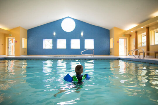 Toddler boy swims alone in indoor pool.