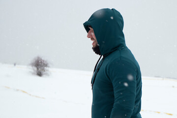 Fototapeta na wymiar guy in green sports raglan on the background of the snowy horizon. Snowfall. The concept of doing sports in snowy weather. High quality photo