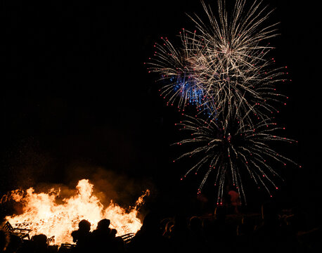 People near big fire between darkness and fireworks in sky
