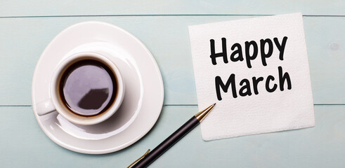 On a light blue wooden tray, there is a white cup of coffee, a handle and a napkin that says HAPPY MARCH