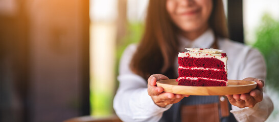 A beautiful young asian woman, waitress or a chef holding and serving a piece of red velvet cake in...