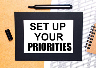 On a wooden table, there is a black open marker, a brown notepad and a sheet of paper in a black...