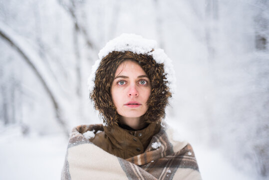 Young girl wrapped in blanket in snowy forest looks straight on