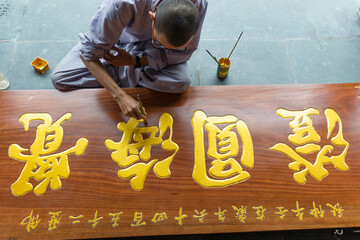cropped image of young monk painting on a wooden board