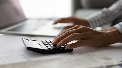 Close up cropped view of young woman accountant auditor doing paperwork at desk full of financial documents control accounting entries check transaction. Focus on female hand pressing calculator keys