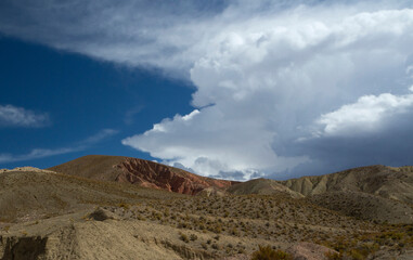 Arid landscape. View of the desert sand, dunes, flora and colorful hills under a beautiful sky with clouds. 