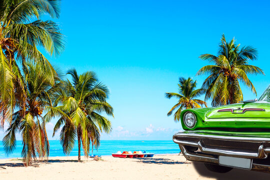 The tropical beach of Varadero in Cuba with green american classic car, sailboats and palm trees on a summer day with turquoise water. Vacation background.