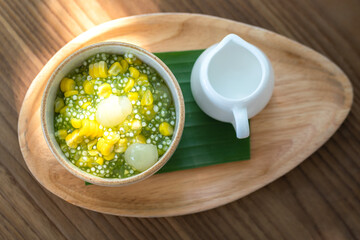 Sago or Saku topping with corn, longan fruits and coconut milk, served in white bowl on the wooden plate. This is one of famous tradition Thai dessert food. Sweet food close-up photo.