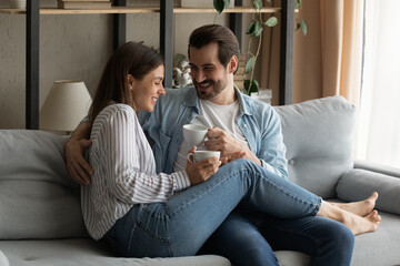 Nothing is better. Affectionate lovers spouses cuddle on couch at living room have pleasure joke...