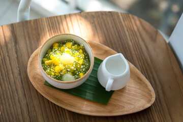 Sago or Saku topping with corn, longan fruits and coconut milk, served in white bowl on the wooden plate. This is one of famous tradition Thai dessert food. Sweet food close-up photo.