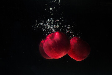 Three red ripe apples fall into the water on a black background