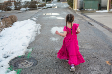 A little girl in a fancy dress struts proudly down a snowy street