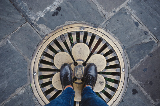 someone standing on a fancy metal manhole cover black shoes and jeans