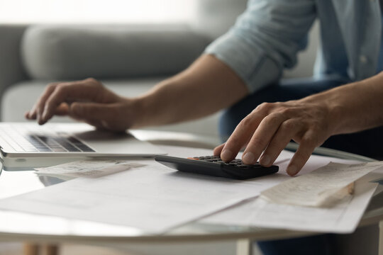 Close up of young male accountant hands make audit of expenses calculate charges based on paper documents. Cropped shot of man bookkeeper work with bills pay fees taxes online using web app on laptop