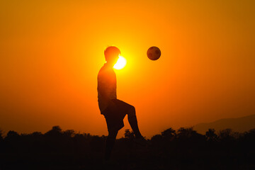 Silhouette action sport outdoors of a young man having fun playing soccer football for exercise in community rural area under the twilight sunset.