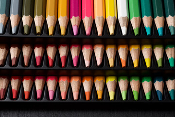 Watercolor pencils lined up in a black plastic box.