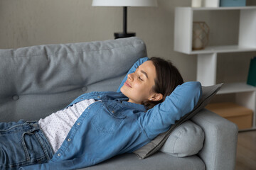 Serene female teenager lying on soft cozy sofa with closed eyes napping having pleasure enjoying...