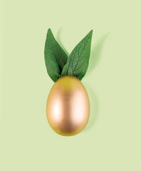 Easter egg painted in gold color with green bunny ears. Happy Easter minimalistic background.