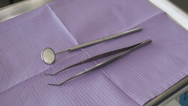 Close-up of a dental tool tray as the dentist places down a mouth mirror and tweezers.