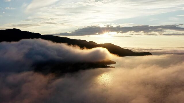 Sunset glow peeking behind the mountains over clouds and waves -aerial