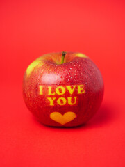 Valentine's Day themed apple with I Love You message and a heart symbol covered in water droplets and placed on a red background