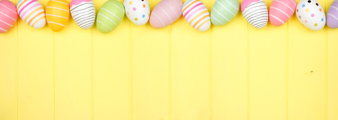 Colorful Easter Egg top border over a soft yellow wood banner background. Overhead view with copy space.