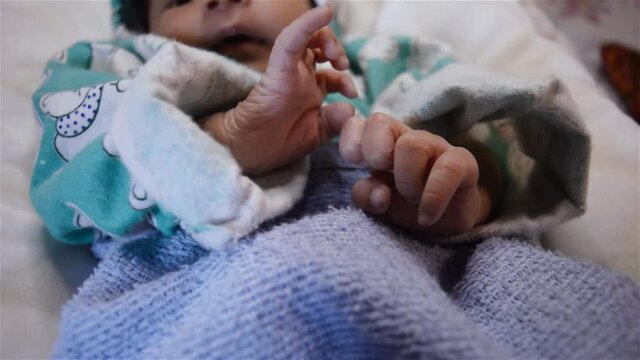 Newborn baby moving arms and legs and fingers while sleeping. Close Up. Beautiful Newborn baby boy closeup lying in bed while wrapped in baby blanket in hospital ward.
