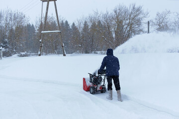 A man using snowblower to clear driveway near residential house during a heavy snowfall. Russia.