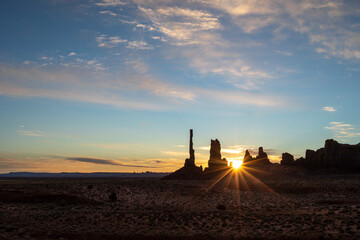 A starburst effect pierces through rock formations at Monument Valley