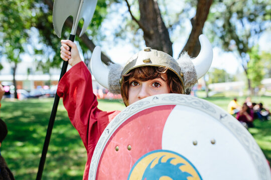 Young teen girl hides her face partially behind viking shield dress up