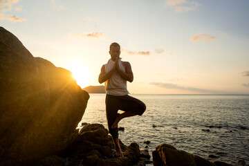 guy doing yoga poses on sharp rocks near the beach in thailand