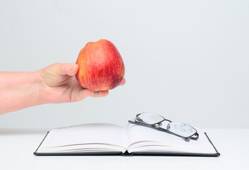 On the open diary are glasses. In a woman's hand is a red apple. Concept-fruit diet, recreation