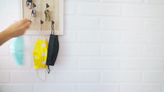 Female hinging the protective face mask and keys on organizer hook on the loft design white background brick wall in the home hallway. Health care concept during COVID-19 pandemic 4K concept footage.