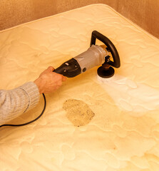 a man cleans a dirty mattress with an electric brush