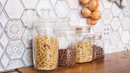 Pasta in glass jars. Pasta on a wooden countertop in a modern bright kitchen.