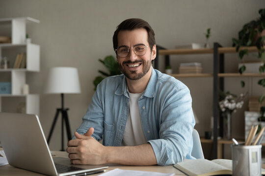 Profile picture of successful man worker employee college university student sitting by work desk at home office looking at camera. Portrait of motivated young guy studying working online using laptop