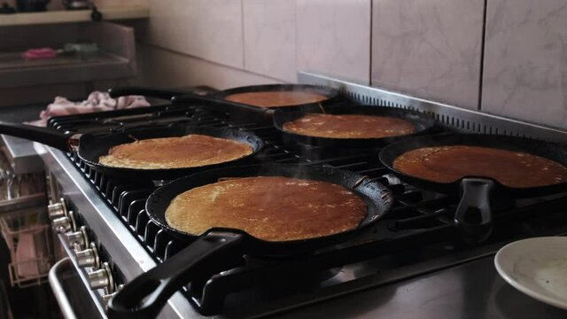Dolly backward on pankakes being cooked on the pans of a gas oven