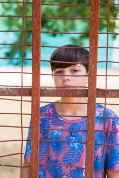 serious teen in casual wear behind metallic fence outdoors