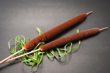 Two bulrushes and green bast lie on a black background.
Zwei Rohrkolben  und grüner Bast liegen...