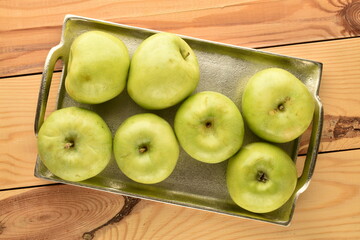 Several ripe green apples with a metal tray on a wooden table, close-up, top view.
