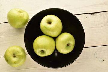 Several ripe green apples in a ceramic bowl on a wooden table, close-up, top view.