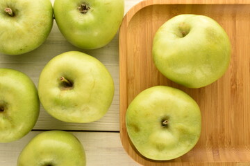 Several ripe green apples in a bamboo dish on a wooden table, close-up, top view.