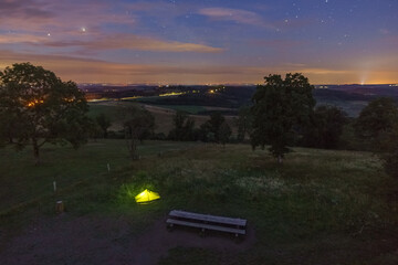 Illuminated green camping tent in resting area from high angle view at night in rural german eifel...