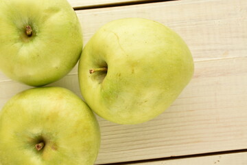Three juicy green apples on a wooden table, close-up, top view.