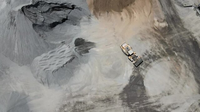 Construction vehicle in sand quarry from above. Aerial drone video tracking front loader carrying load of sand.