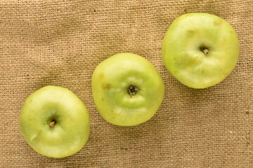 Three ripe green apples on burlap, close-up, top view.
