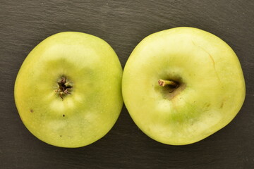 Two ripe green apples on a slate board, close-up, top view.