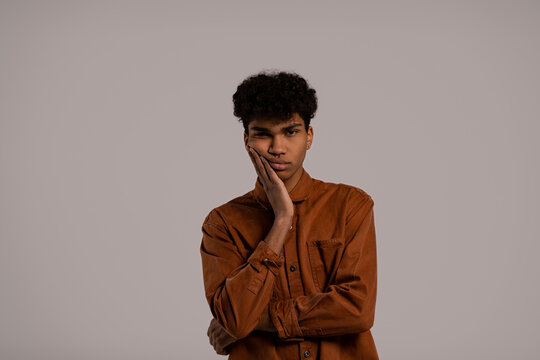 Photo of black man looks bored and not interested in something. Male wears shirt, isolated grey color background