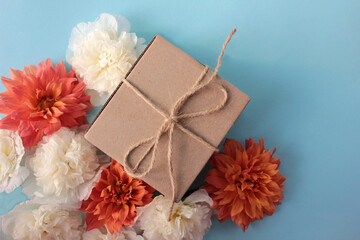 Kraft gift box with flowers on colored backdrop. Flat lay composition with present package, orange dahlia and white mallow flowers on blue background. 